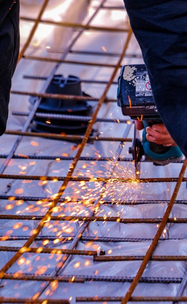A construction worker skillfully cuts steel with an angle grinder, creating flying sparks outdoors.